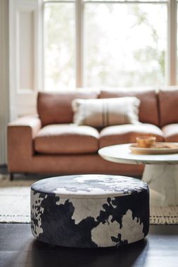 DFS Vegan Willow three-seater sofa in tan Woodland Plain leather look fabric, with DFS Vegan Freedom footstool in black cow Vegan Accent fabric